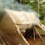 Photo of a bathhouse in the forest made from scrap materials: film on poles and a fire in the stones